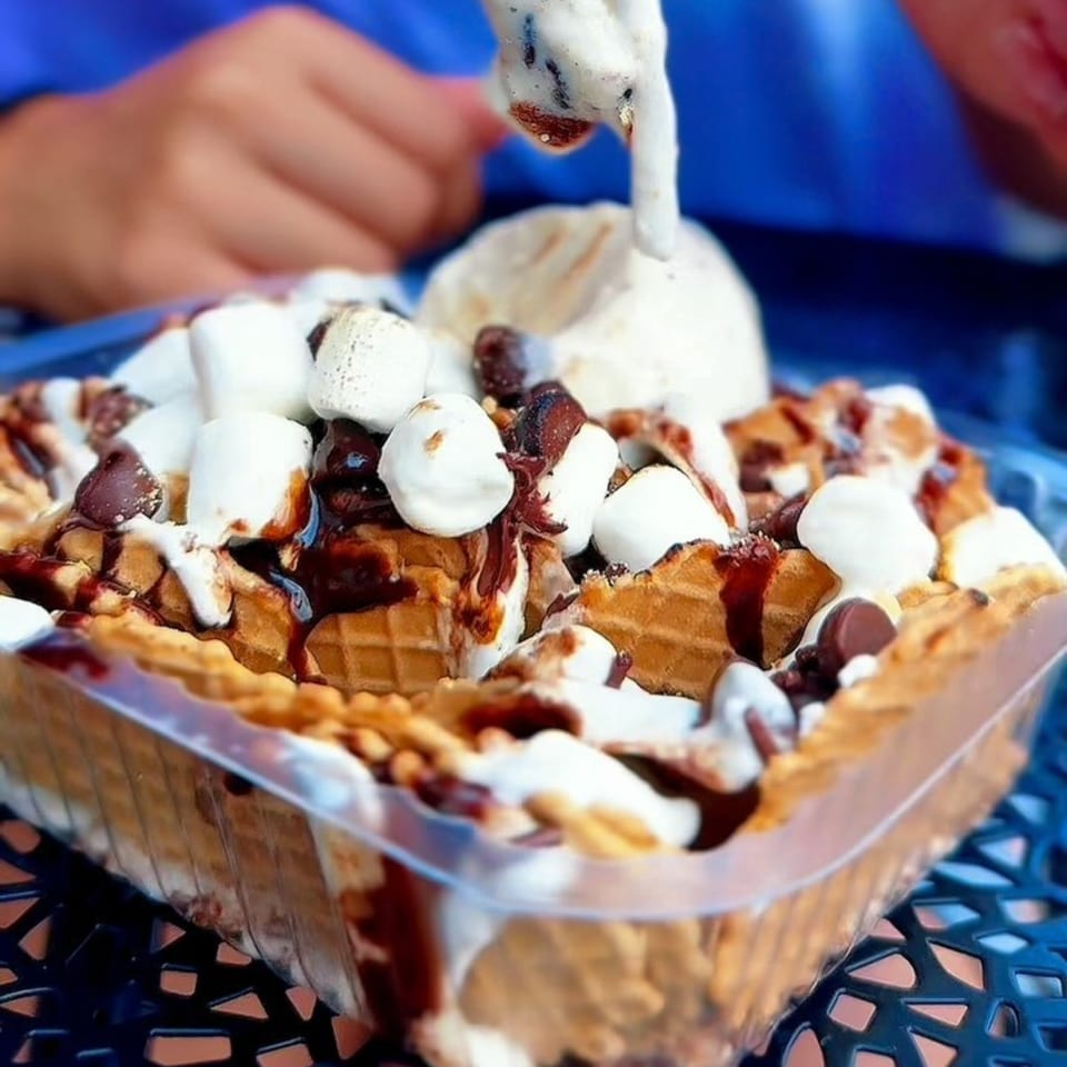 A waffle bowl filled with marshmallows, chocolate, and ice cream, with a spoon scooping some.
