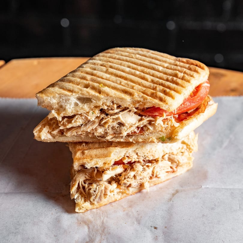Two halves of a grilled chicken and tomato panini stacked on parchment paper.