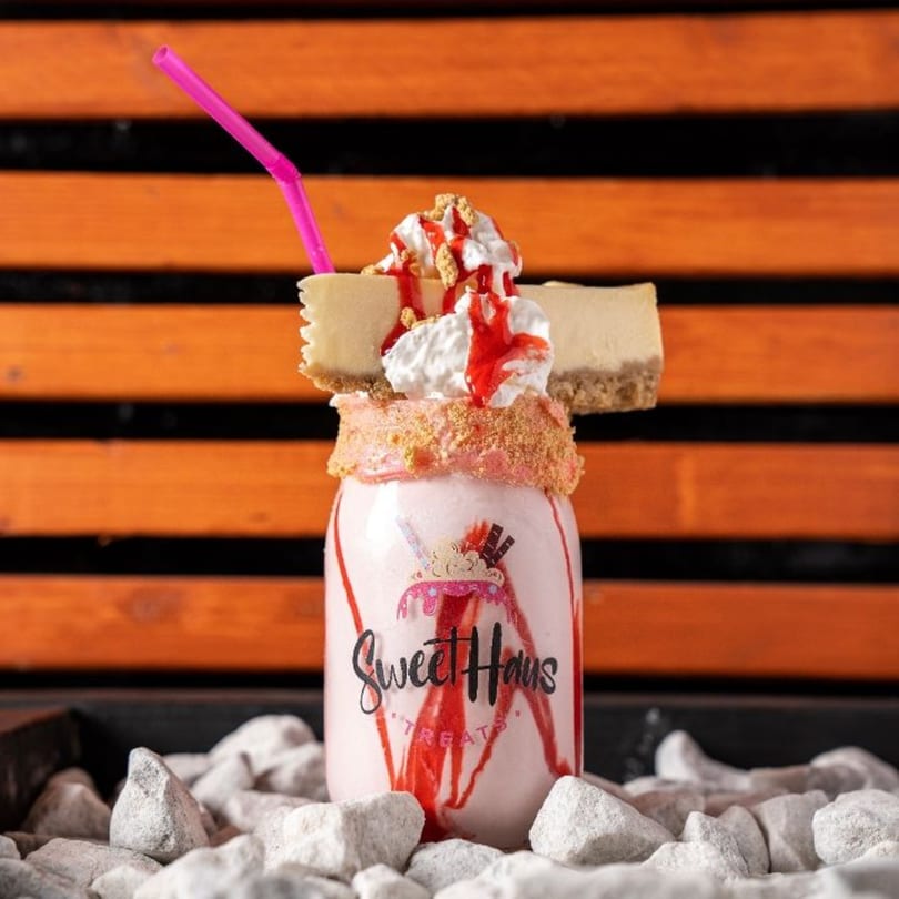 A Sweethaus Treats strawberry milkshake topped with cheesecake slices, whipped cream, and strawberry drizzle.