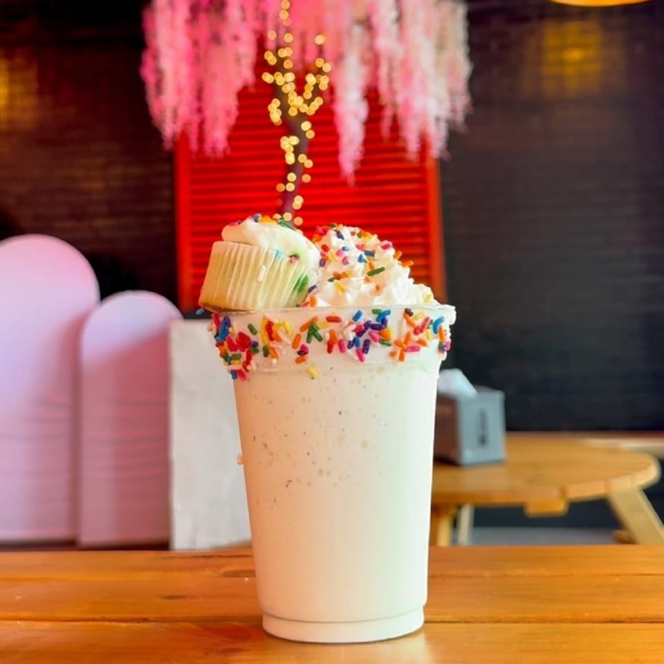 A Sweethaus Treats milkshake topped with whipped cream, sprinkles, and a mini cupcake.