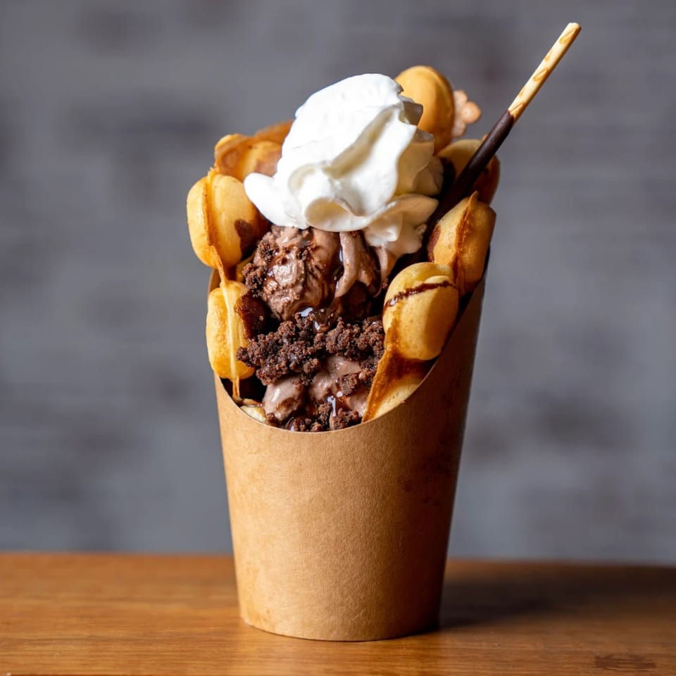 A Sweethaus Treats bubble waffle cup filled with chocolate ice cream, whipped cream, and a cookie stick.