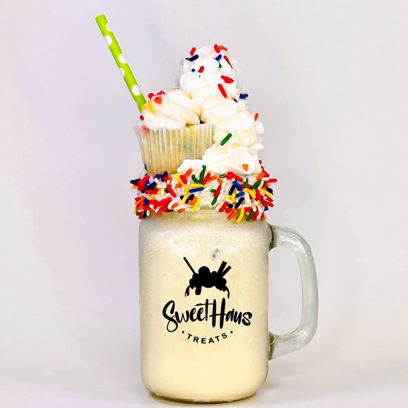 A Sweethaus Treats milkshake in a mason jar, topped with whipped cream, sprinkles, and a cupcake.