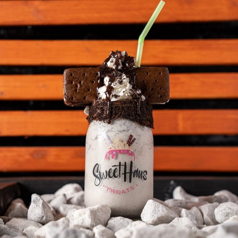 A Sweethaus Treats cookies and cream milkshake with whipped cream, chocolate syrup, and two cookie sandwiches.